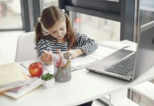 Dziewczynka w domu odrabia lekcje przy laptopie i zeszytach
